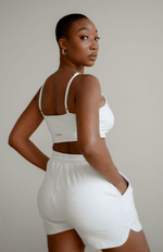 Woman wearing a white sports bra and shorts on a plain background