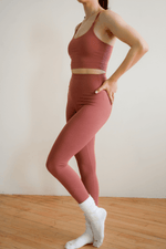 Person wearing a pink athletic outfit standing on a wooden floor with a white wall background