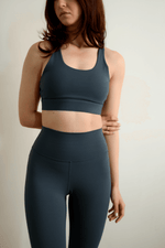 Woman wearing a dark green sports bra and leggings set against a plain background
