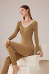 Woman wearing a brown bodysuit sitting on a white chair against a plain background