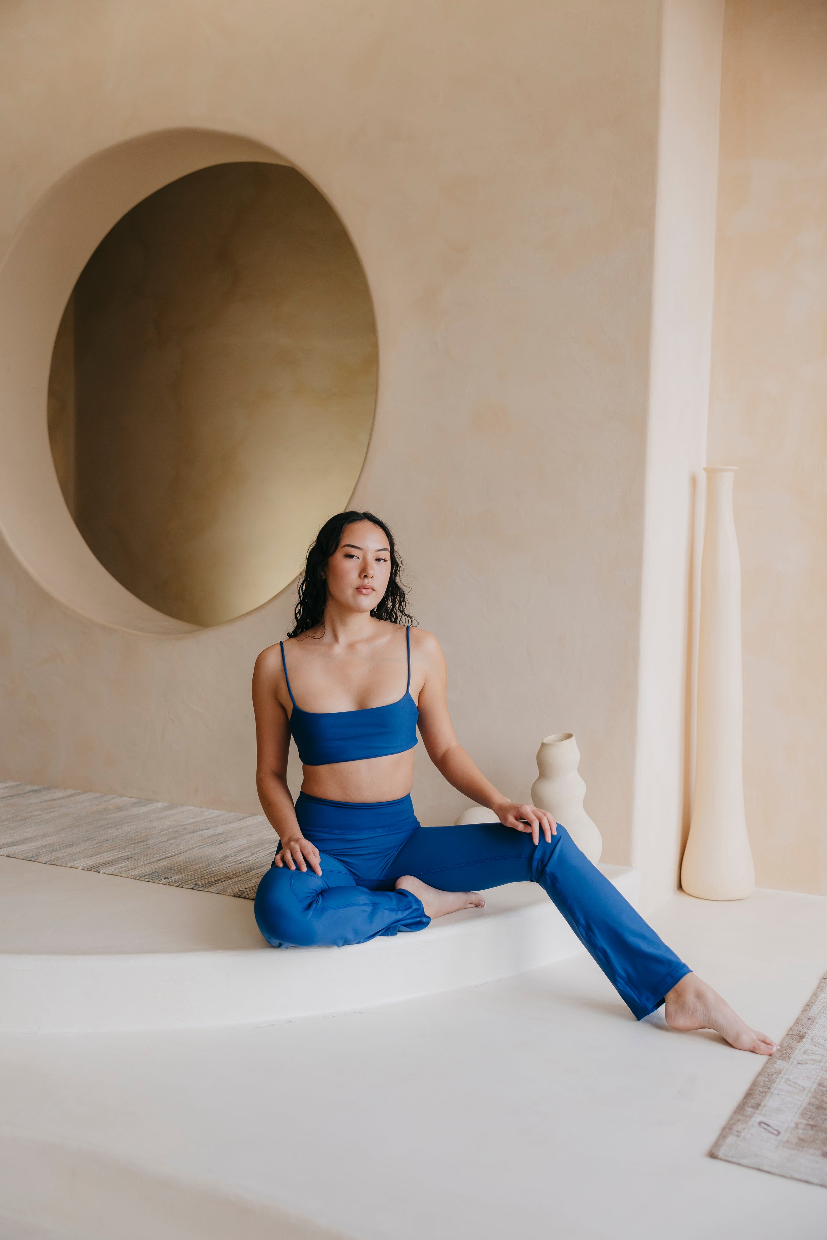 Woman in blue athletic wear sitting on a white rug in a room with a circular alcove.