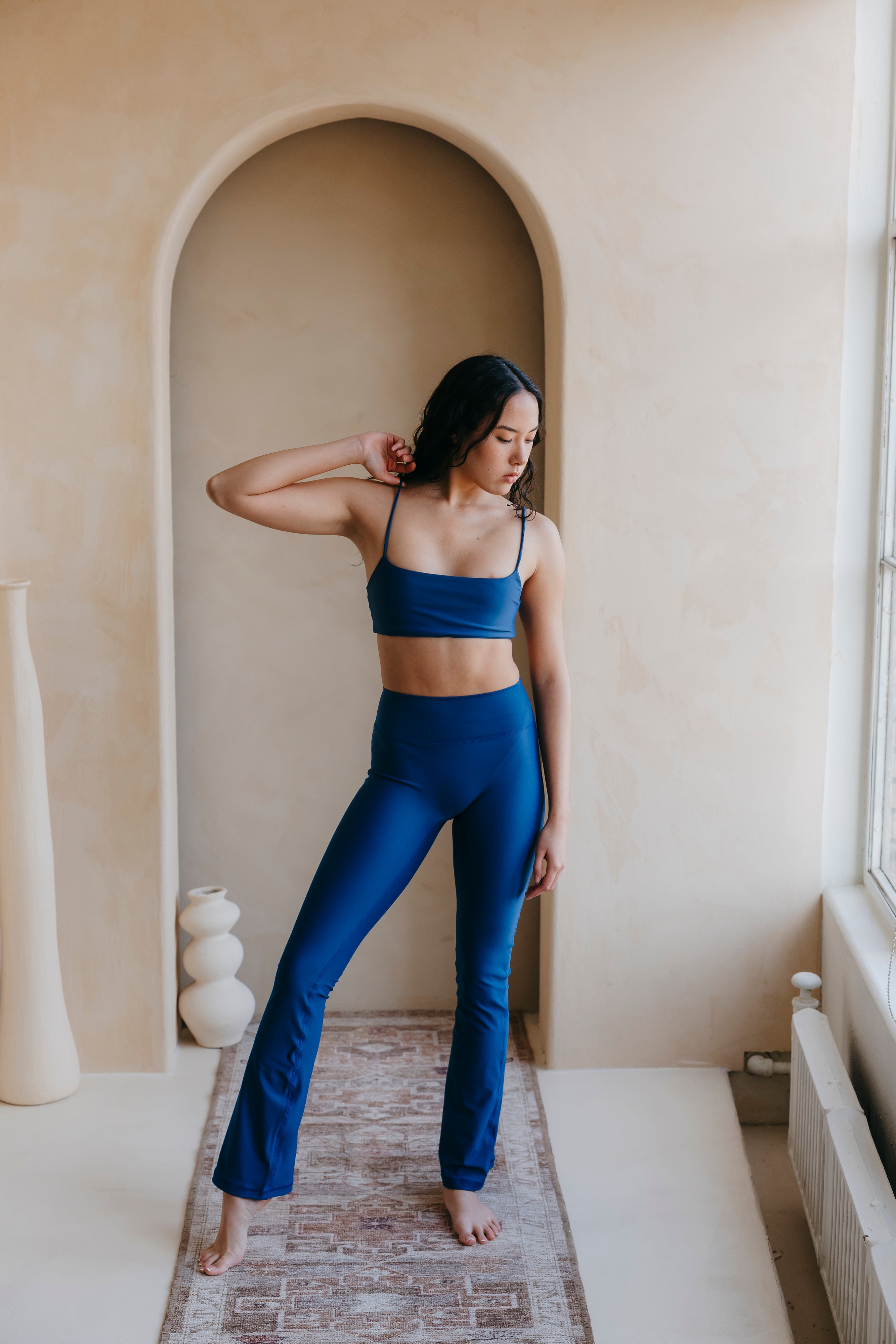 Woman in blue athletic wear standing in a room with neutral walls and a window.