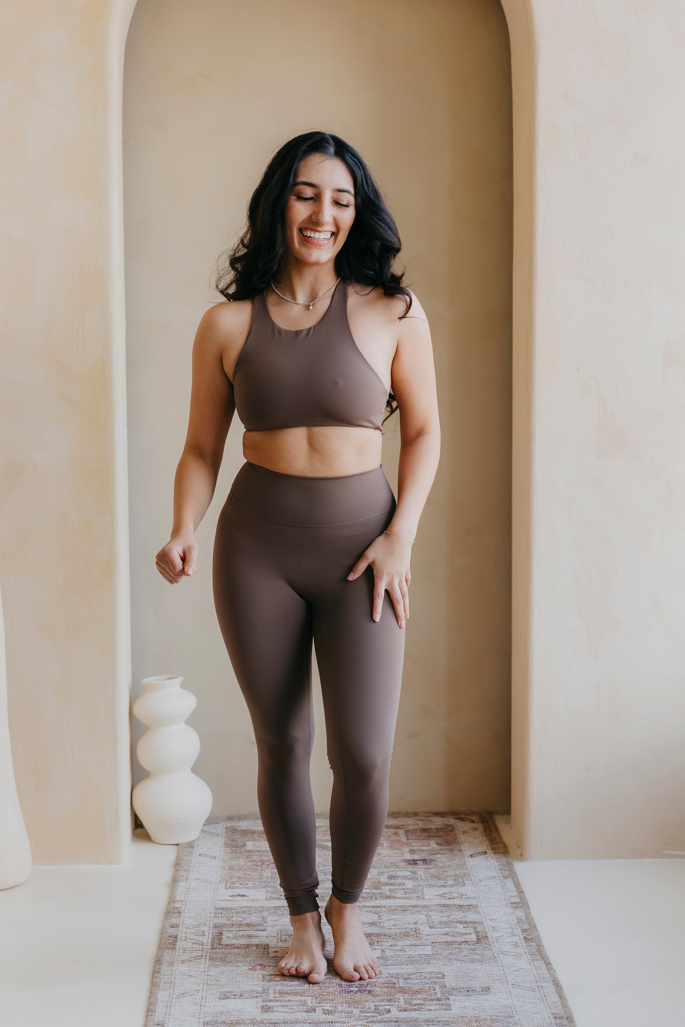 Woman in brown athletic wear standing in a room with an archway.