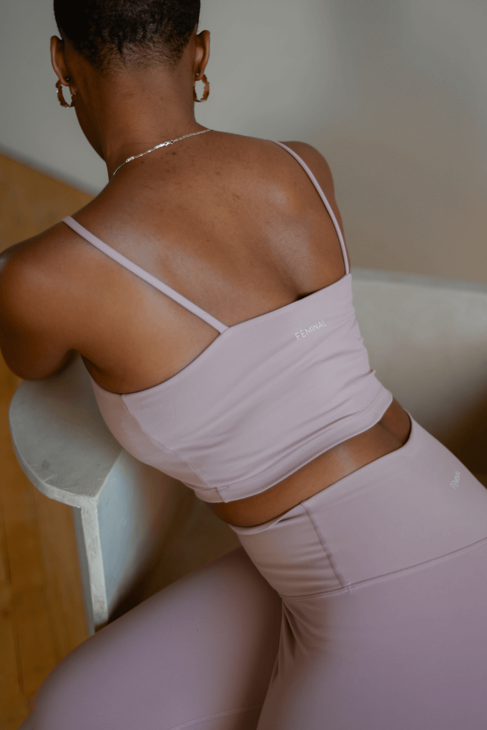 Person wearing a light pink top and pants sitting on a white chair.