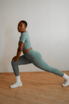 Person wearing a green athletic outfit stretching on a wooden floor.
