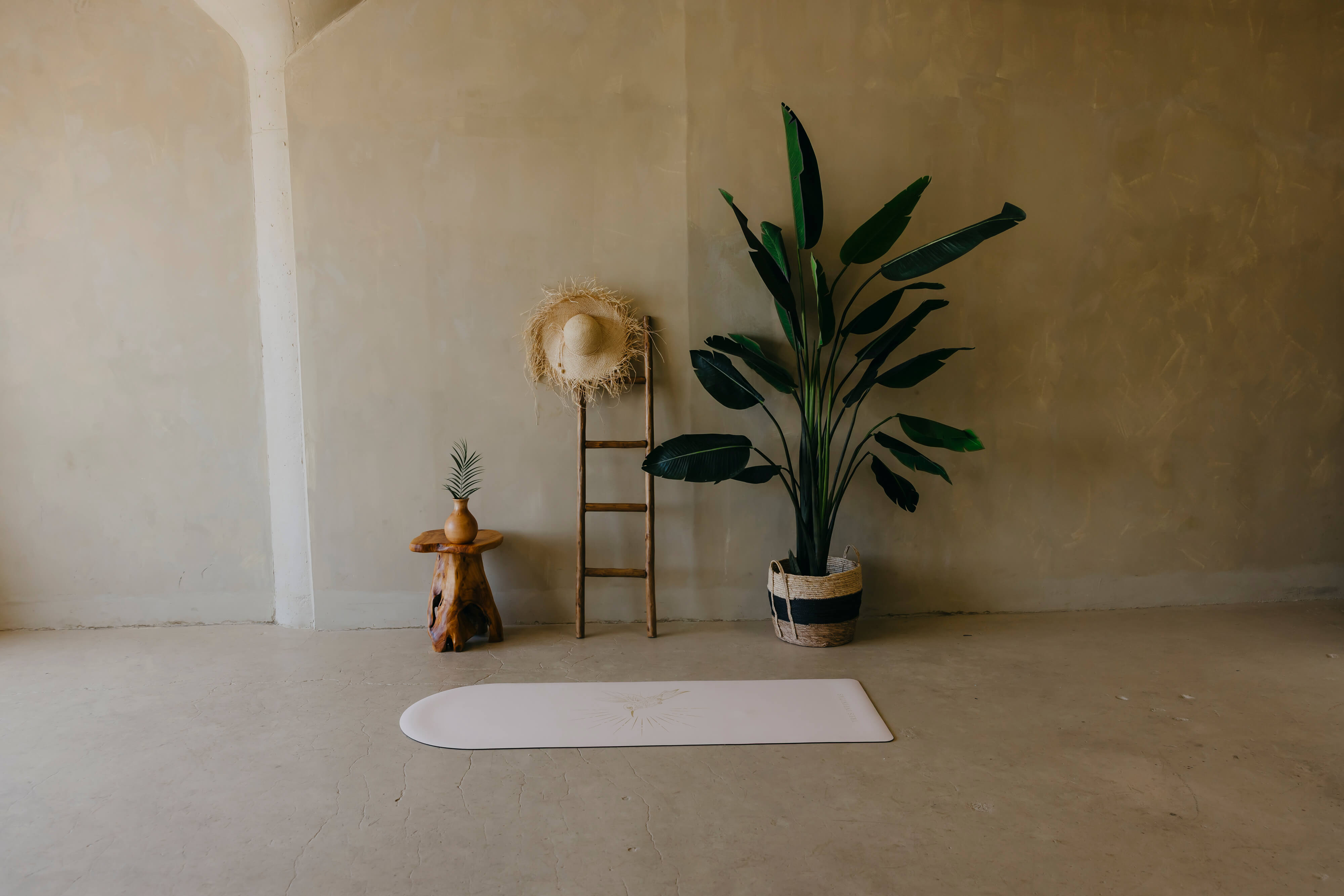Yoga mat on a concrete floor with decorative items and a plant against a plain wall.